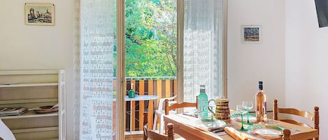 A dining area with a wooden table, chairs, and a view of greenery through open curtains.