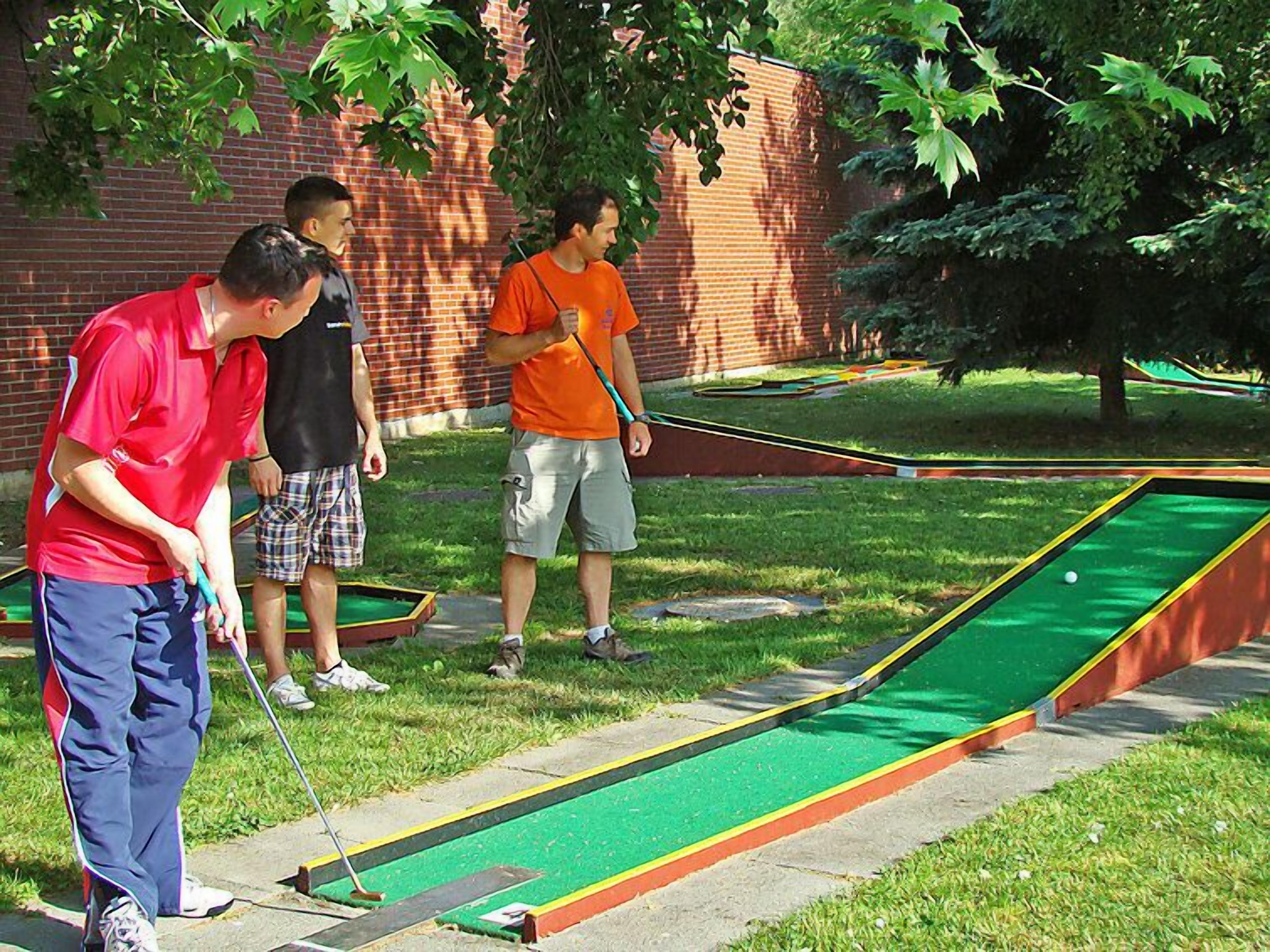 A group of people playing croquet in an outdoor setting with a brick wall and trees in the background.