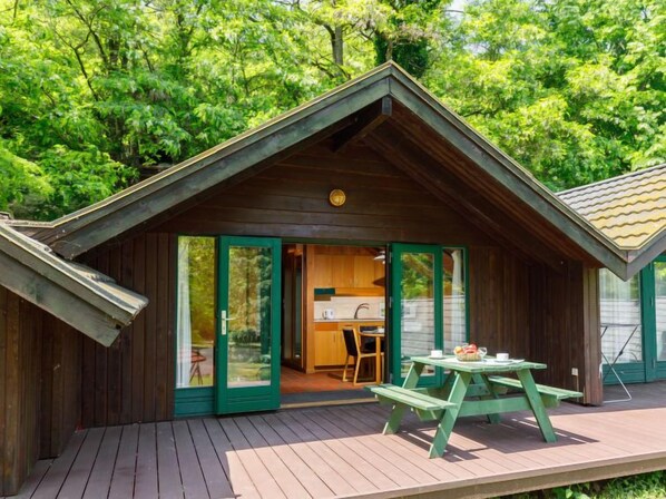 A wooden cabin with a deck, a kitchen area, and a picnic table.