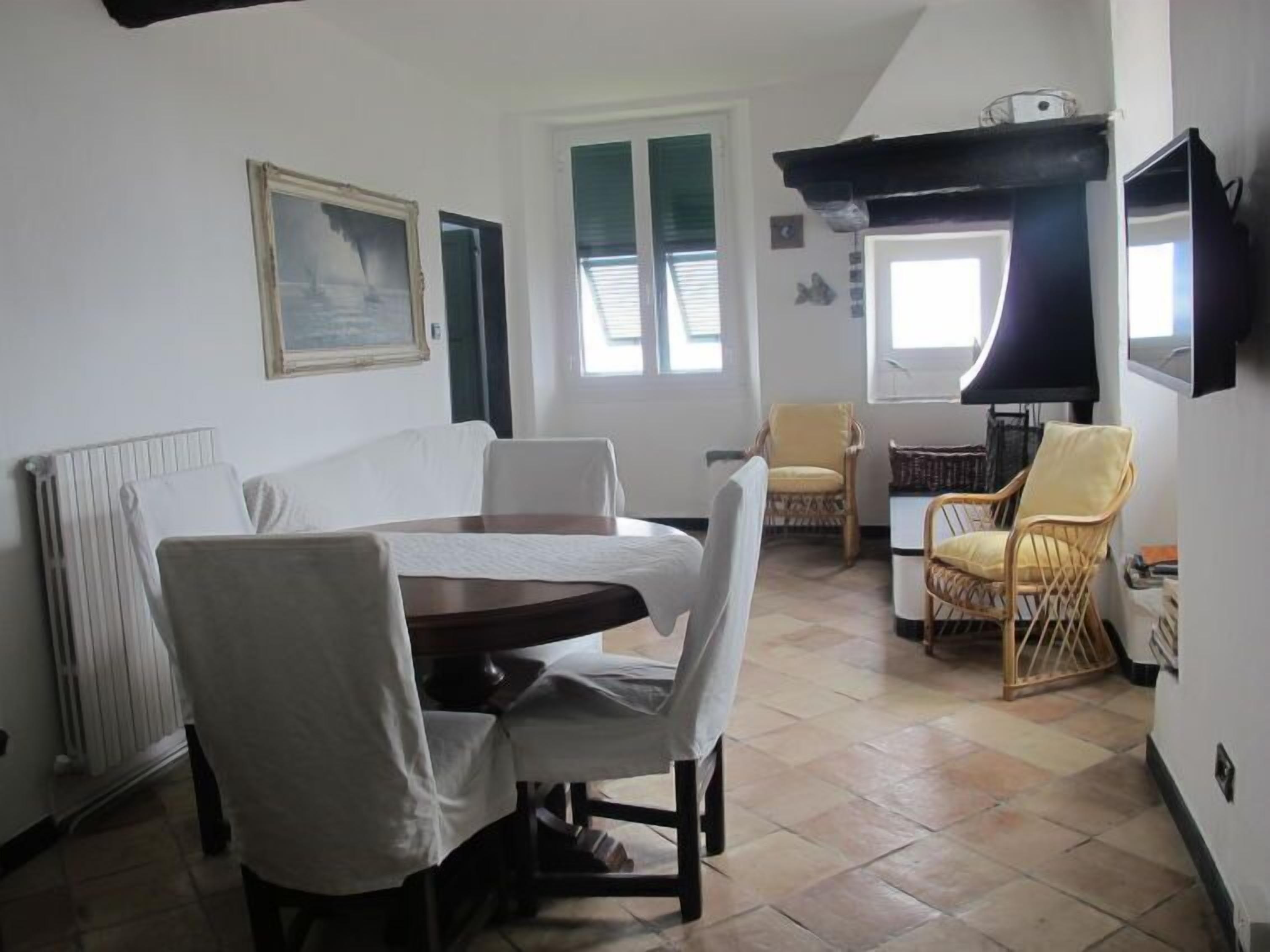 A dining area with a table and chairs, a radiator, a window with blinds, a television, and a chair with a cushion.