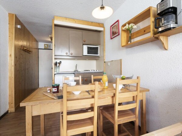 A compact kitchen with wooden cabinets, a microwave, and a coffee machine on a shelf.