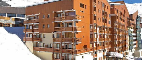 Un hotel moderno a più piani con balconi e lo sfondo di una località sciistica.
