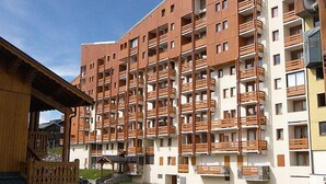 Ein mehrgeschossiges Wohnhaus mit Balkonen, einem Parkplatz und einem kleinen Garten.