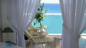 A bedroom with a bed, a nightstand, a lamp, and a view of the ocean through sheer curtains. - Golden Life by Interhome (Jávea)