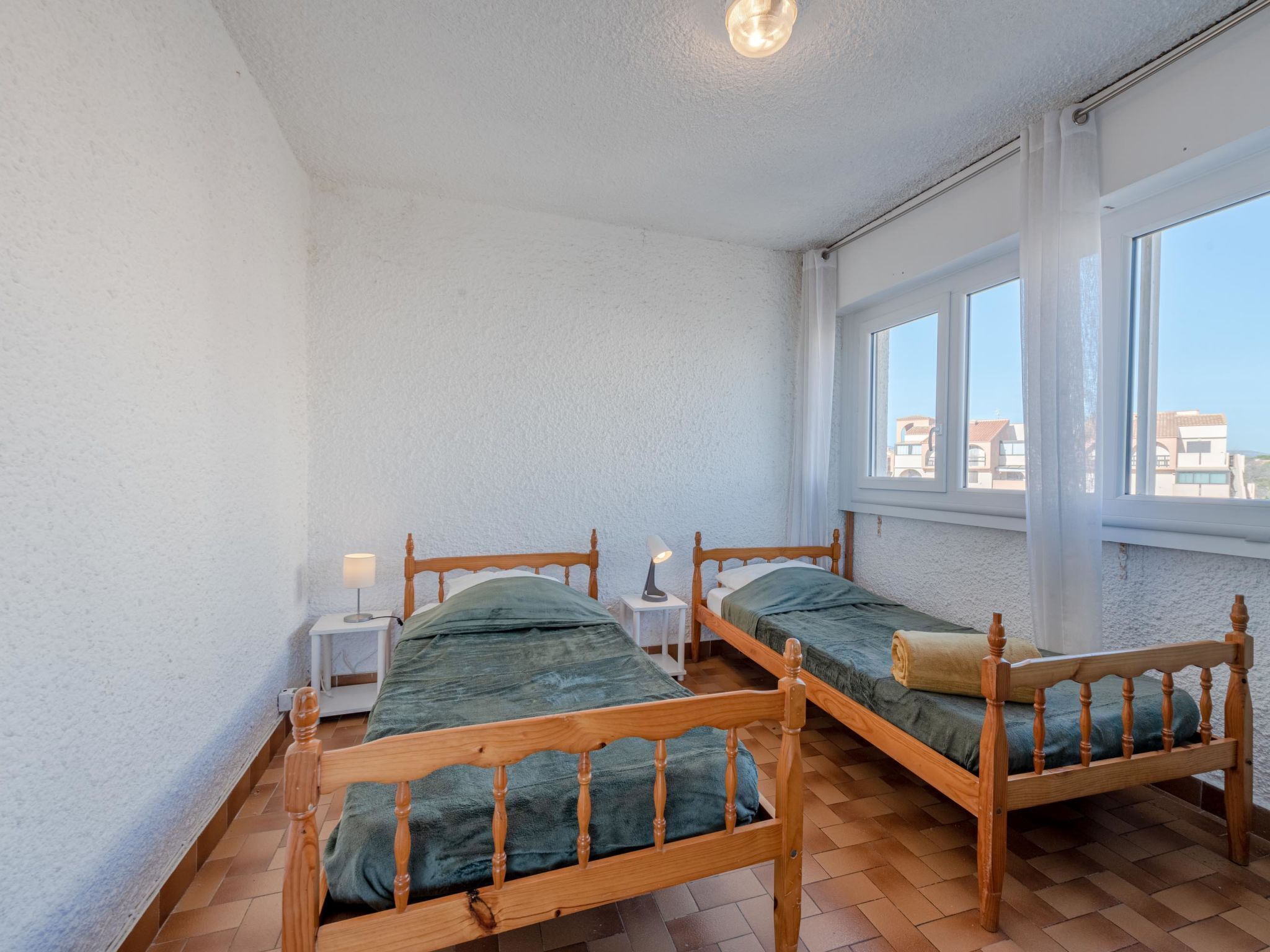 A room with two wooden beds, white walls, and a large window providing a view of buildings.