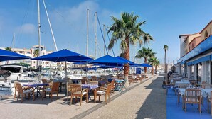 Een jachthaven met boten, blauwe parasols en terrasplekken.