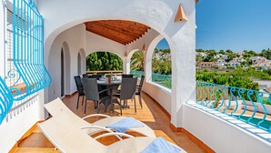 A covered outdoor seating area with a table and chairs, a pool, and a view of a hillside town. - Vacation home Luisa by Interhome (Calpe/Calp)