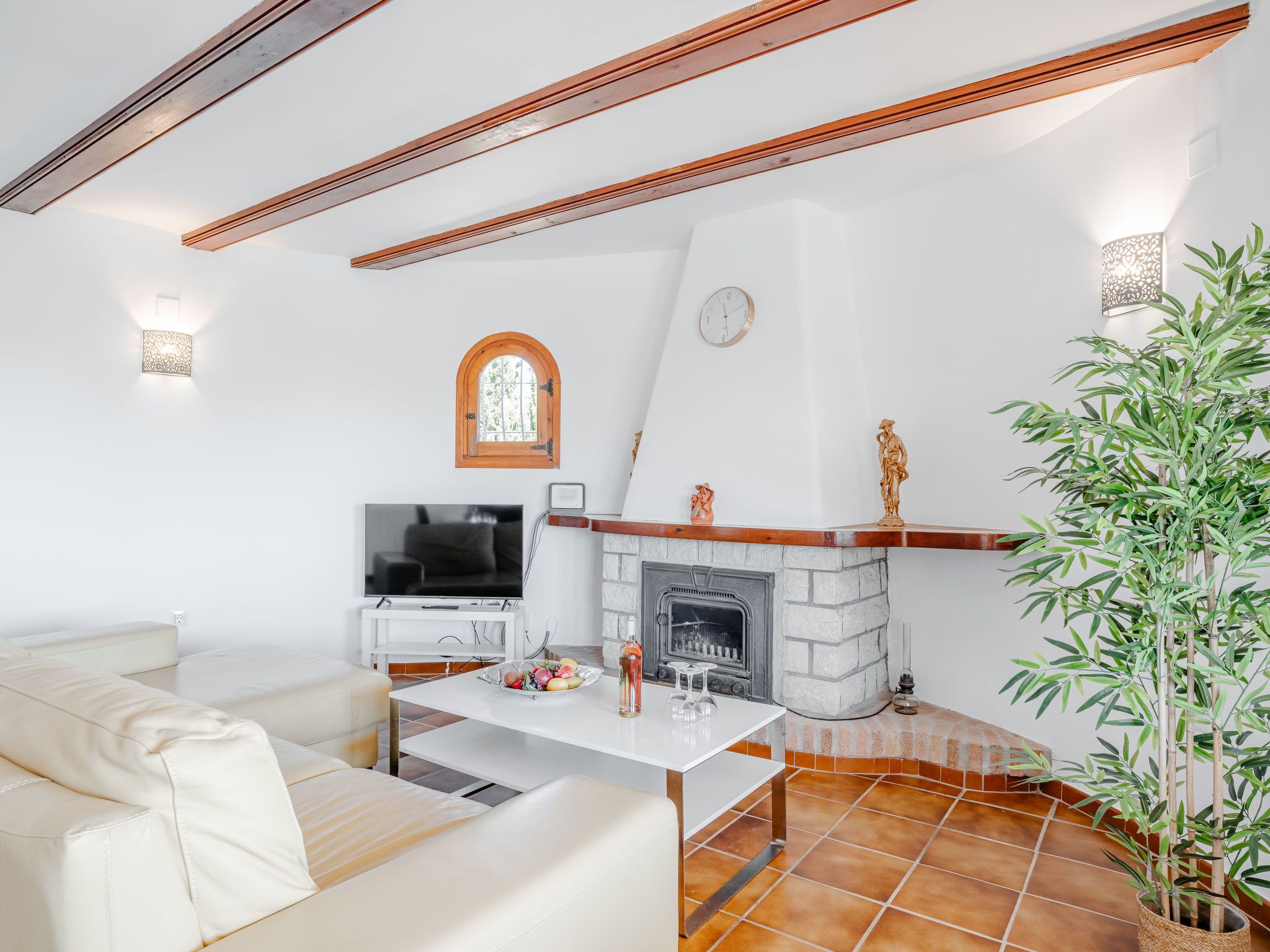 A living room with a white sofa, a TV, a fireplace, and a potted plant.