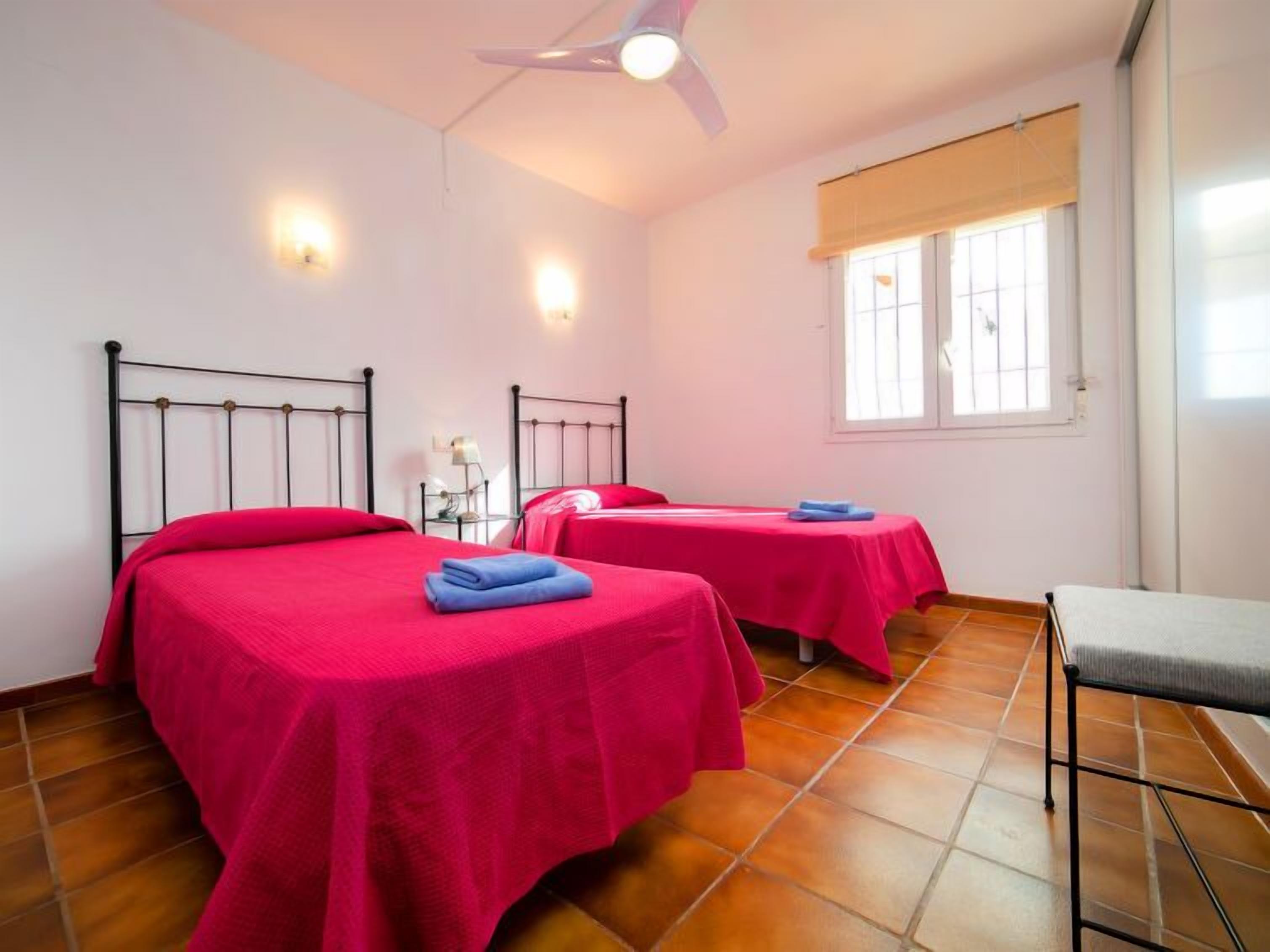 Une chambre avec deux lits, un ventilateur de plafond et une fenêtre avec des stores.