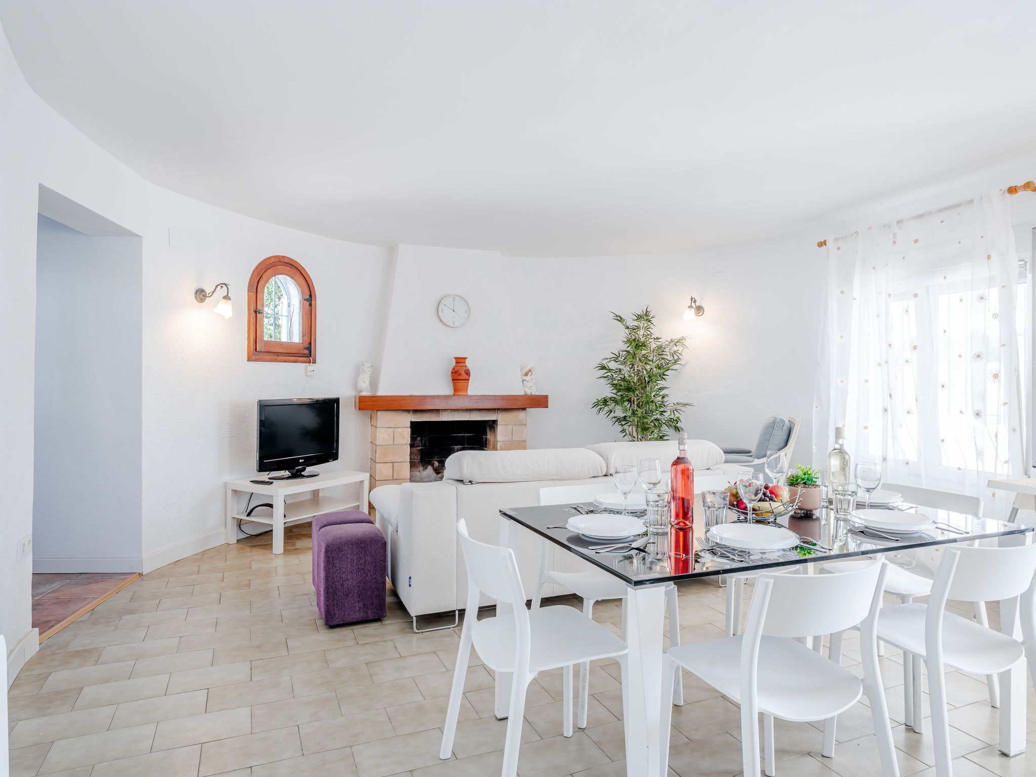 A modern living room with a fireplace, white furniture, and a dining area with a glass table.