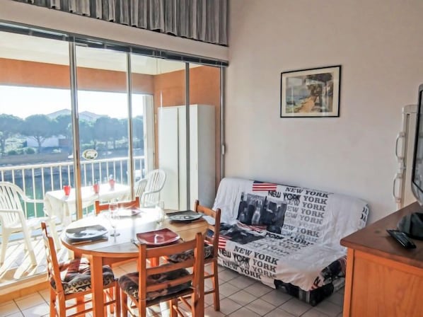 Ein Balkon mit Tisch und Stühlen, einer mit einer Decke bedeckten Couch und einem gerahmten Bild an der Wand.