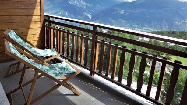 A balcony with wooden railings and two lounge chairs with leaf-patterned cushions.