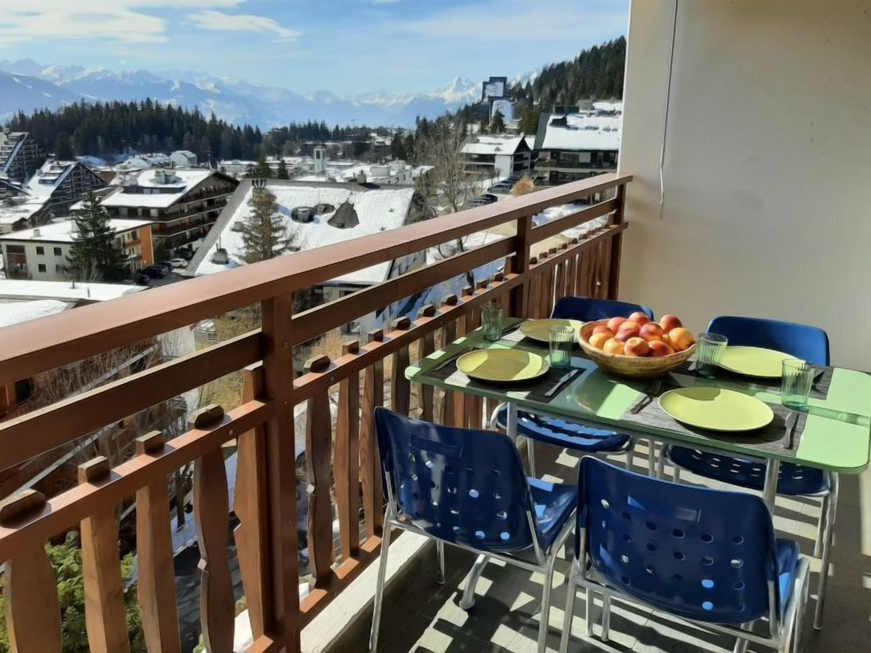 Un balcón con una mesa dispuesta para dos personas, con vistas a un pueblo montañoso.