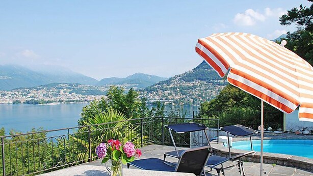 A patio with a stone table, chairs, a striped umbrella, and a vase of flowers. - Vacation home Ursula by Interhome (Pugerna)
