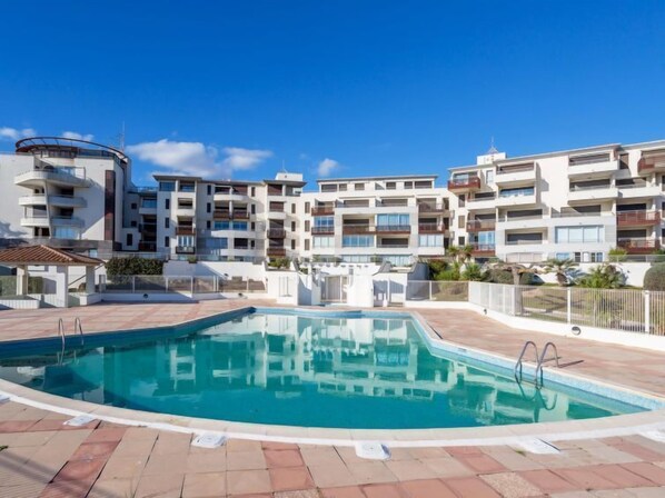 Un moderno complejo de apartamentos con piscina, balcones y un cielo azul despejado.