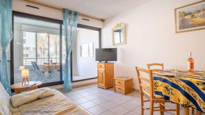 Een slaapkamer met een bed, een televisie, een eettafel met stoelen en een raam met gordijnen.