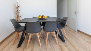 Un espace repas moderne avec une table ronde, six chaises noires et un saladier à fruits.