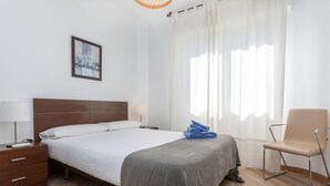 Une chambre d’hôtel bien rangée, avec un lit, des tables de chevet, une chaise et une fenêtre avec des rideaux.