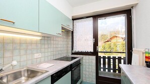 A compact kitchen with a sink, dishwasher, and a window overlooking a balcony. - Marignac 33 by Interhome (Villars)