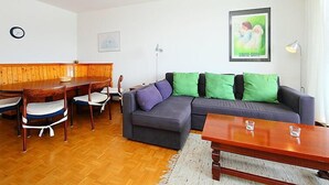 A living room with a wooden dining table, chairs, a sofa with green and purple cushions, a coffee table, and a framed picture on the wall. - Marignac 33 by Interhome (Villars)