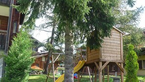 A wooden playhouse with a slide, surrounded by a wooden fence and greenery. - Apartment Diana by Interhome (Münster)
