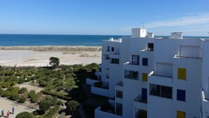 Un edificio moderno bianco con numerosi balconi affacciati su una spiaggia e l'oceano.