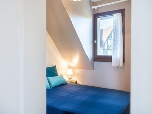 Un dormitorio pequeño y acogedor con techo inclinado, una cama individual, una mesita de noche con lámpara y una ventana con cortinas.