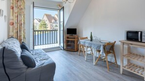 A modern apartment with a dining area, a sofa, a TV, and a balcony with a view of buildings. - Fleur Marine by Interhome (Cabourg)