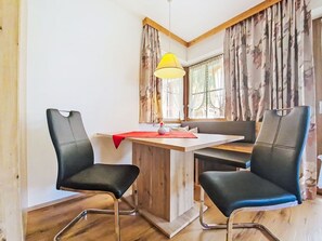 A room with two black chairs, a wooden table, a yellow hanging lamp, and a window with floral curtains.
