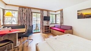 Et værelse med seng, skrivebord med stol, sofa, fjernsyn og et vindue med gardiner.