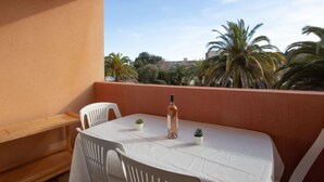 Un balcone con tavolo bianco, due sedie, una bottiglia e piccoli vasi con piante.