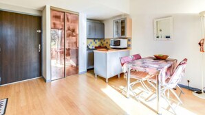A modern kitchen with a microwave, cabinets, and a small island. There is a dining area with a table and chairs. - Val des Chênes by Interhome (Cavalaire)