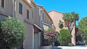 A row of Mediterranean-style buildings with stucco walls and terracotta roofs, surrounded by lush greenery and a clear blue sky. - Val des Chênes by Interhome (Cavalaire)