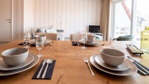 A dining area with a wooden table set for four, including bowls, glasses, and cutlery. - Zandloper II with balcony by Interhome (Bredene)