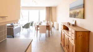 A modern kitchen and dining area with a large window, a dining table set for four, and a wooden cabinet with drawers. - Zandloper II with balcony by Interhome (Bredene)