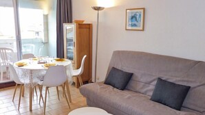 A living room with a grey sofa, a small white table, and a dining table set for four. - Les Balcons de la Méditerranée by Interhome (Narbonne-Plage)