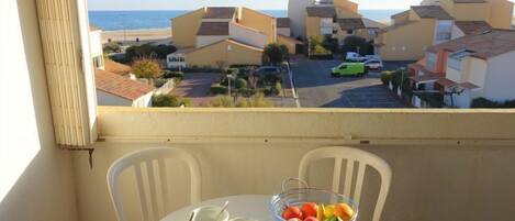 A balcony with a table set for tea, a fruit bowl, and a view of a coastal neighborhood.