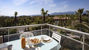 A balcony with a table set for breakfast, overlooking a lush landscape with palm trees and distant mountains. - Les Capitelles by Interhome (Saint Cyprien)