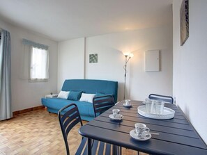 Une pièce avec un canapé bleu, une table à manger avec des chaises et un lampadaire.