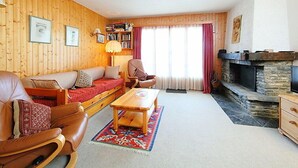 Uma sala de estar acolhedora com parede de madeira, um sofá, uma poltrona, uma mesa, uma lareira e uma estante de livros.
