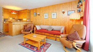 Uma sala de estar acolhedora com um sofá, duas cadeiras, uma mesa de centro e um espaço de cozinha com armários de madeira e um balcão.