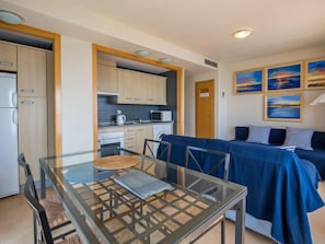 A compact kitchen with modern appliances, a dining area with a glass table, and a living space with a sofa and artwork.