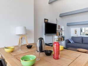 Ett modernt vardagsrum med ett matbord i trä, en soffa, en tv som är monterad på väggen och en bokhylla.