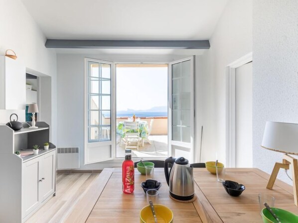 A modern kitchen with a view of the sea, a dining area with a table set for two, and a balcony with a table and chairs.