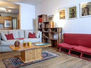 A cozy living room with a sofa, a red couch, a wooden coffee table, and a bookshelf.