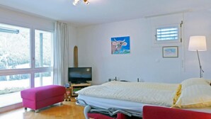 A hotel room with a bed, a TV, a window with curtains, a painting, and a lamp. - Silence Apt. H by Interhome (Wengen)