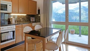 A modern kitchen with wooden cabinets, a black countertop, and a dining area with a glass table and white chairs. - Silence Apt. H by Interhome (Wengen)