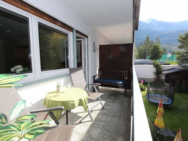 Un balcon avec une table et des chaises, un banc, un trampoline et une vue sur les montagnes.