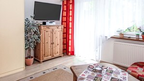 A cozy living room with a television, wooden cabinet, potted plant, and a table with a decorative tablecloth. - Am Birkenhain by Interhome (Seefeld in Tirol)