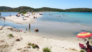 Ein Strand mit klarem Wasser, Menschen beim Schwimmen und Sonnenbaden sowie einigen Sonnenschirmen.